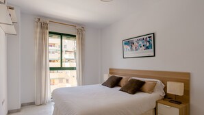 Een net opgemaakt bed met een houten hoofdbord, een nachtkastje met een lamp, en een lijst met een afbeelding aan de muur.