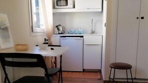 Cocina compacta con gabinetes blancos, microondas y cafetera. Cuenta con un pequeño comedor con mesa y sillas.