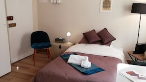 Una habitación de hotel con cama, escritorio, silla, lámpara y una mesita.