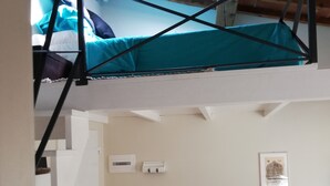 Un dormitorio estilo loft con una cama litera, un sofá, una mesita y un ventanal con vistas al cielo.