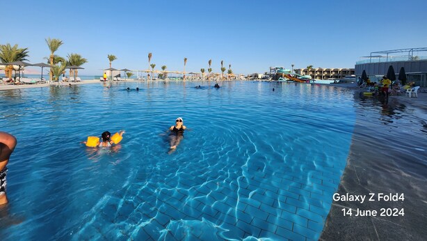 Una piscina con gente, palmeras y un tobogán.