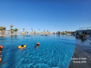 Una piscina con gente, palmeras y un tobogán.