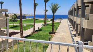 Un balcón con vista al mar, palmeras y un edificio moderno de diseño geométrico.