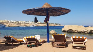 Una playa con sillas de descanso y un gran parasol tejido.