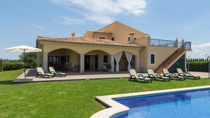 Una casa de dos pisos con piscina, un porche cubierto y una escalera que lleva a un balcón.