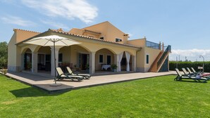 Una casa de dos pisos con un porche cubierto, mobiliario exterior y una escalera que conduce al nivel superior.