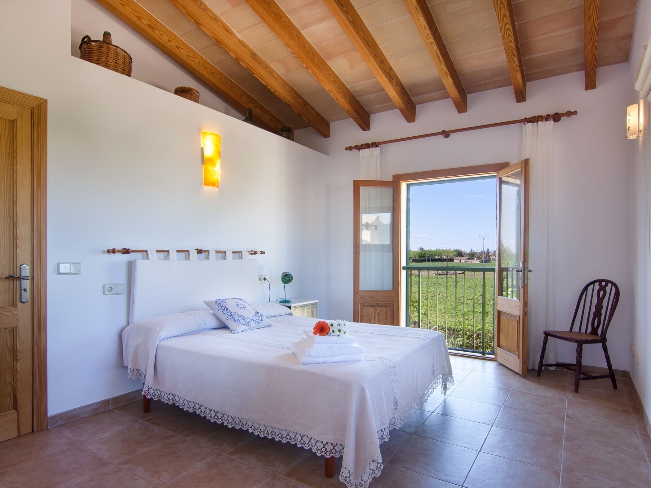 A bedroom with a bed, a nightstand, a chair, and a balcony with a view.