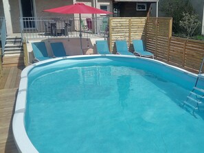 Ein Swimmingpool mit blauem Wasser, umgeben von einer Holzterrasse und Liegestühlen.