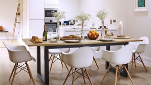 A modern dining area with a wooden table, white chairs, and a hanging light fixture.