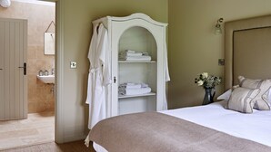 A bedroom with a bed, a wardrobe, a bathroom visible through an open door, and a vase with flowers on the bedside table.