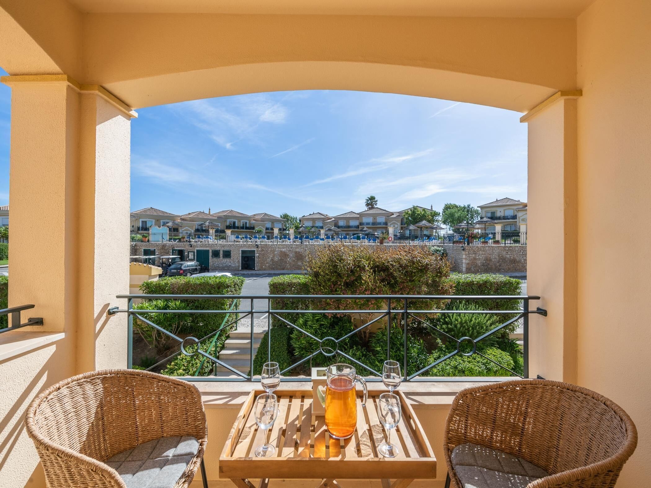 Un balcón con sillones de mimbre, una mesa con bebidas y vista a una zona residencial.