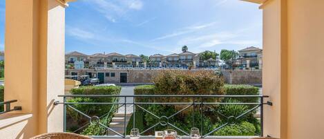 Un balcón con sillones de mimbre, una mesa con bebidas y vista a una zona residencial.