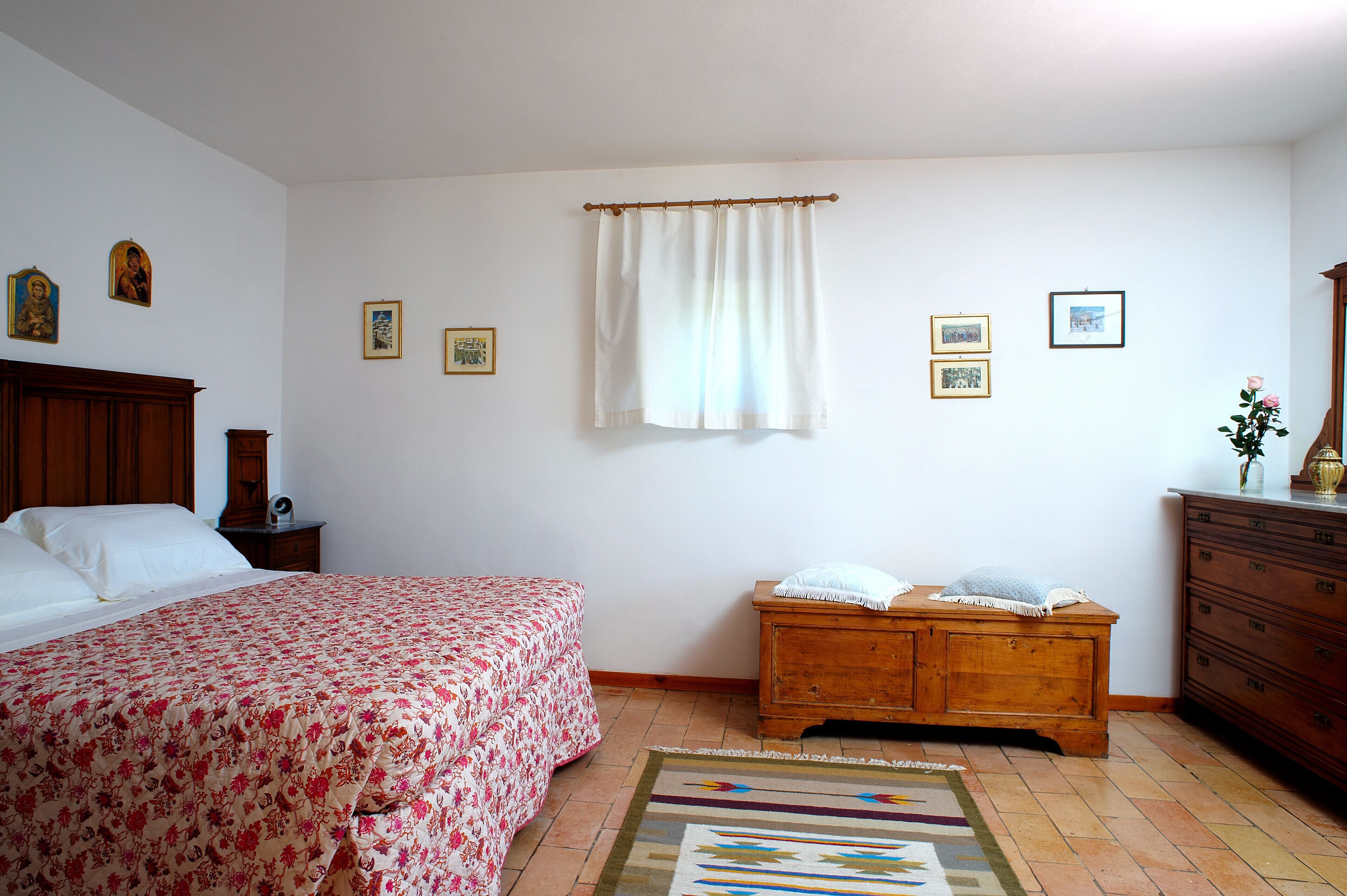 Un dormitorio con una cama, un aparador de madera, una mesita de noche y una ventana con cortinas.