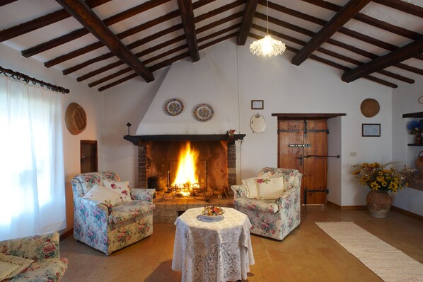 A cozy living room with a fireplace, floral armchairs, a table with a plate, and a wooden door.