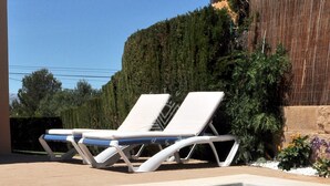 Área de piscina com duas espreguiçadeiras e uma piscina revestida em azulejos.