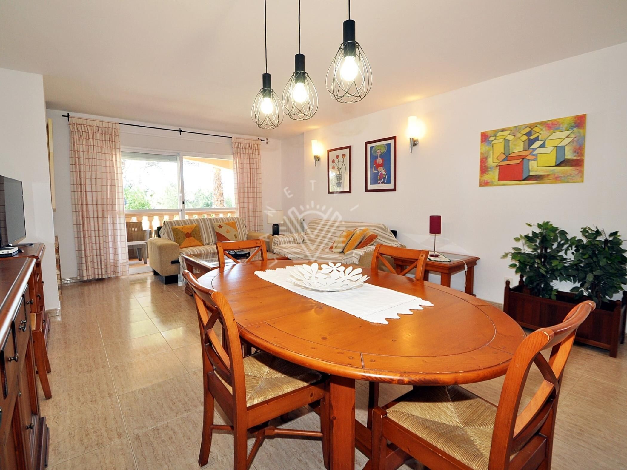Zona pranzo con tavolo e sedie in legno, televisione e vista all'esterno tramite un'ampia finestra.