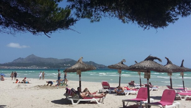 Uma praia com espreguiçadeiras e guarda-sóis de palha, céu limpo e montanhas ao longe.