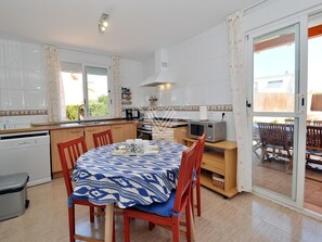 A modern kitchen with white cabinets, a dining table with a blue patterned tablecloth, and a sliding glass door leading to an outdoor area.