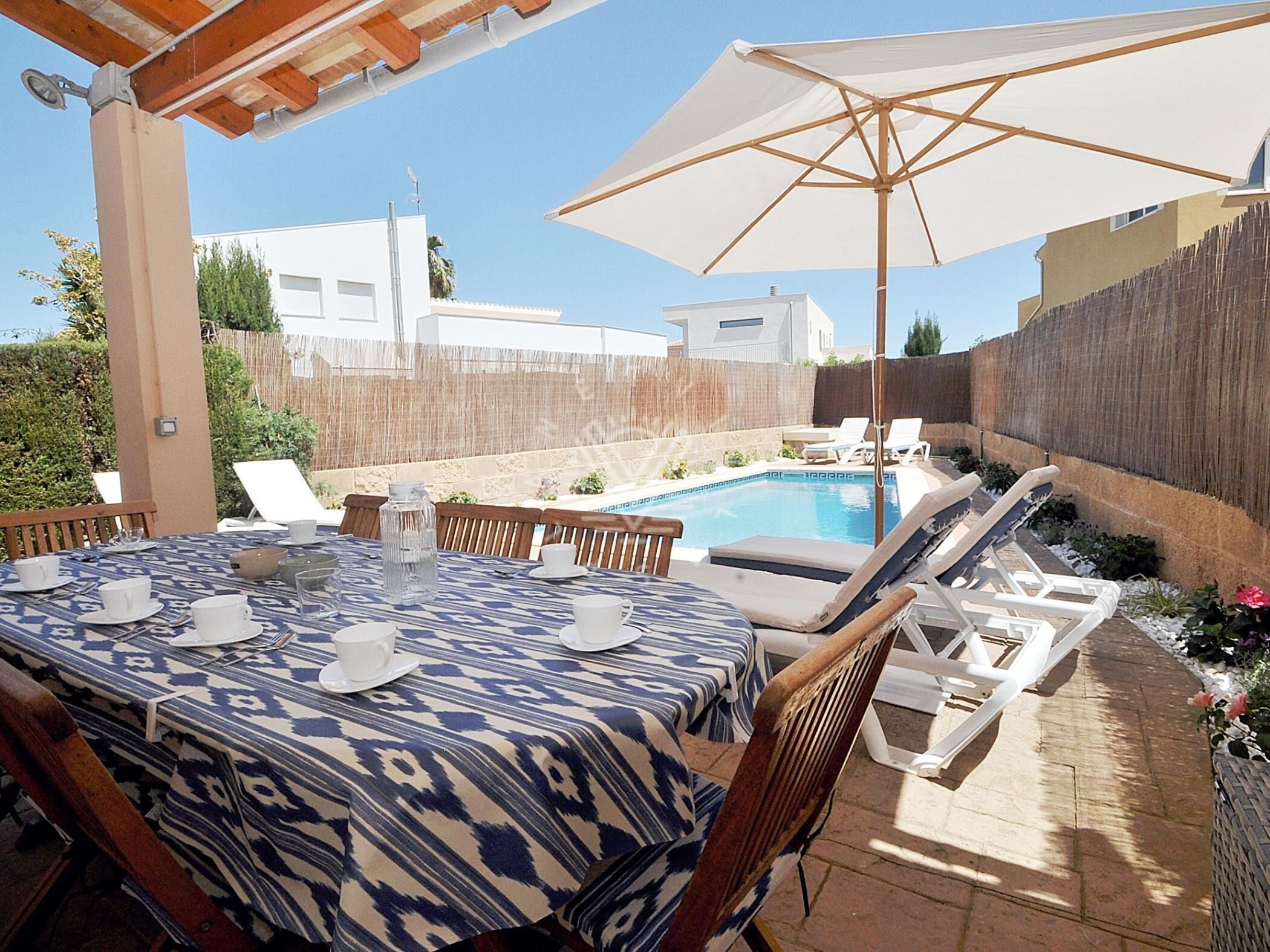 Une terrasse avec une piscine, des sièges d’extérieur et un espace abrité avec un parasol.