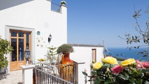 Un edificio bianco con un balcone, un vaso grande con una pianta e vista sul mare.