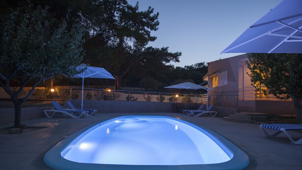 Ein Pool mit beleuchtetem Rand, umgeben von Liegestühlen und Sonnenschirmen, mit einem Gebäude im Hintergrund.
