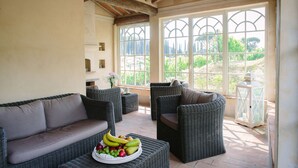 A sunlit room with wicker furniture, a fruit bowl, and large windows offering a view of greenery. - Delicious Villa with wellness center and private pool (Camaiore)