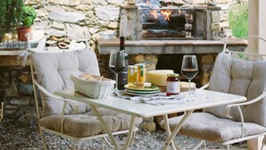 An outdoor patio with a stone fireplace, two cushioned chairs, a table with a basket of bread, a bottle of wine, and a glass of wine. - Delicious Villa with wellness center and private pool (Camaiore)