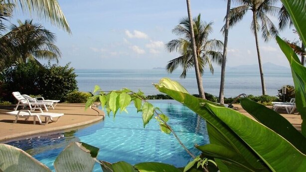 A pool area with lounge chairs and palm trees, overlooking a body of water. - luxury in paradise (Koh Samui)