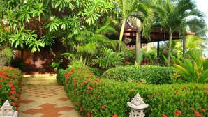 A garden pathway leading to a building with a tiled floor and surrounded by lush greenery and red flowers. - luxury in paradise (Koh Samui)