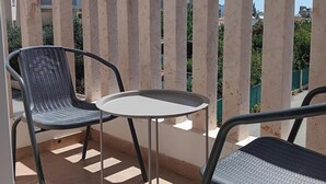 Varanda com duas cadeiras e uma mesa pequena, delimitada por um corrimão branco.
