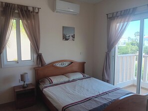 A bedroom with a bed, a nightstand, an air conditioner, a window with curtains, and a balcony.