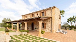A two-story stone house with a covered patio, potted plants, and a lawn.