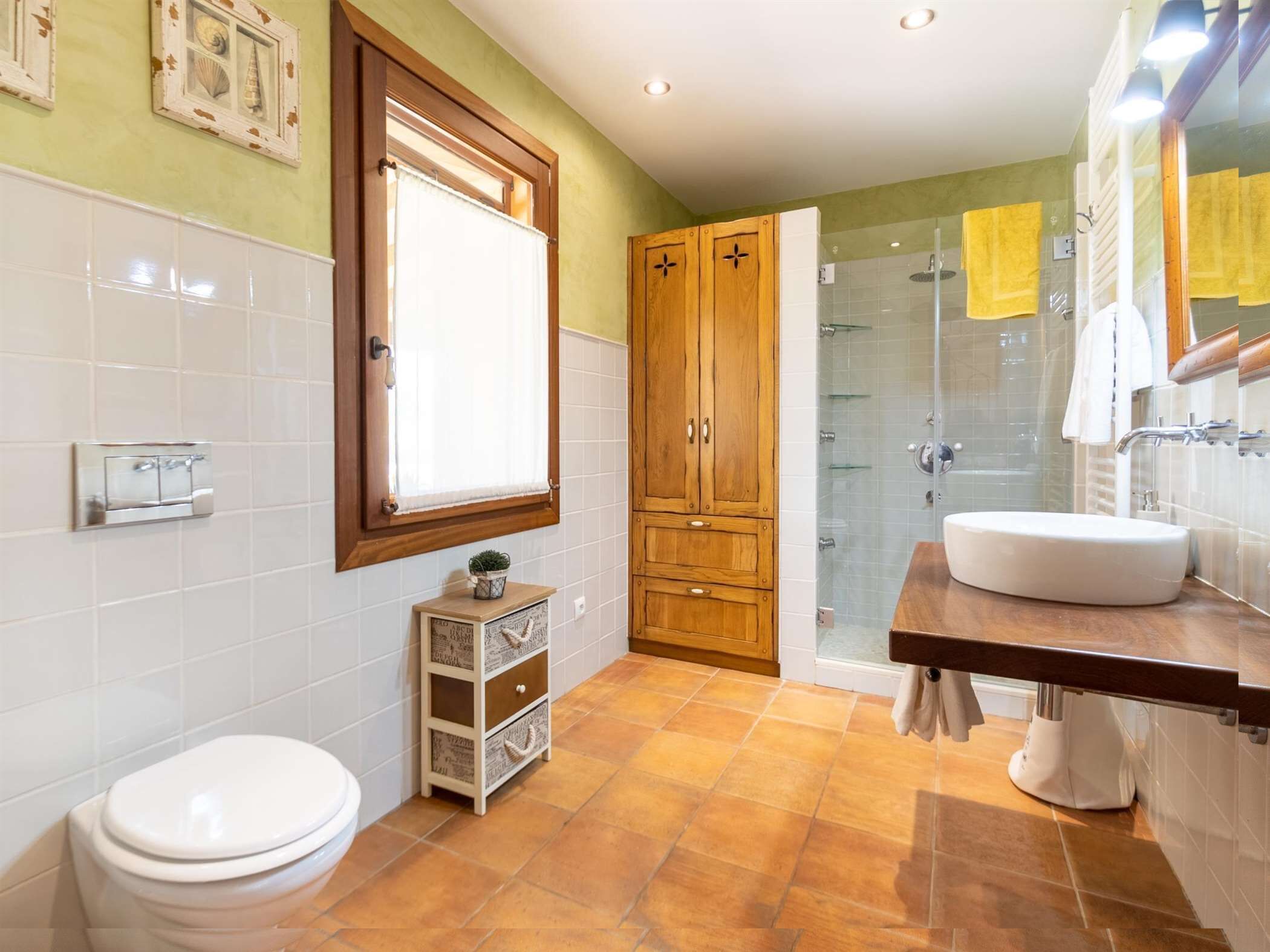 Ein Badezimmer mit Toilette, Holzschränken, einer Duschkabine aus Glas und einem Waschbecken.