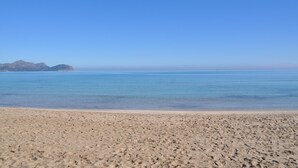 A beach with clear blue water and distant mountains.