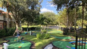 Un campo de mini golf con varias pistas, rodeado de vegetación y una valla.
