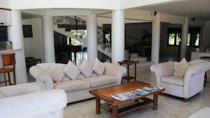 A spacious living area with a beige sofa, a wooden coffee table with magazines, and a staircase with a wrought iron railing.