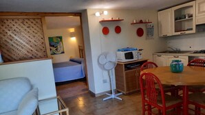 Een ruimtelijk ingerichte leefruimte met een bed, een eettafel met stoelen, een kitchenette en een ventilator.