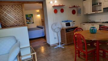 A compact living space with a bed, a dining table with chairs, a kitchenette, and a fan.