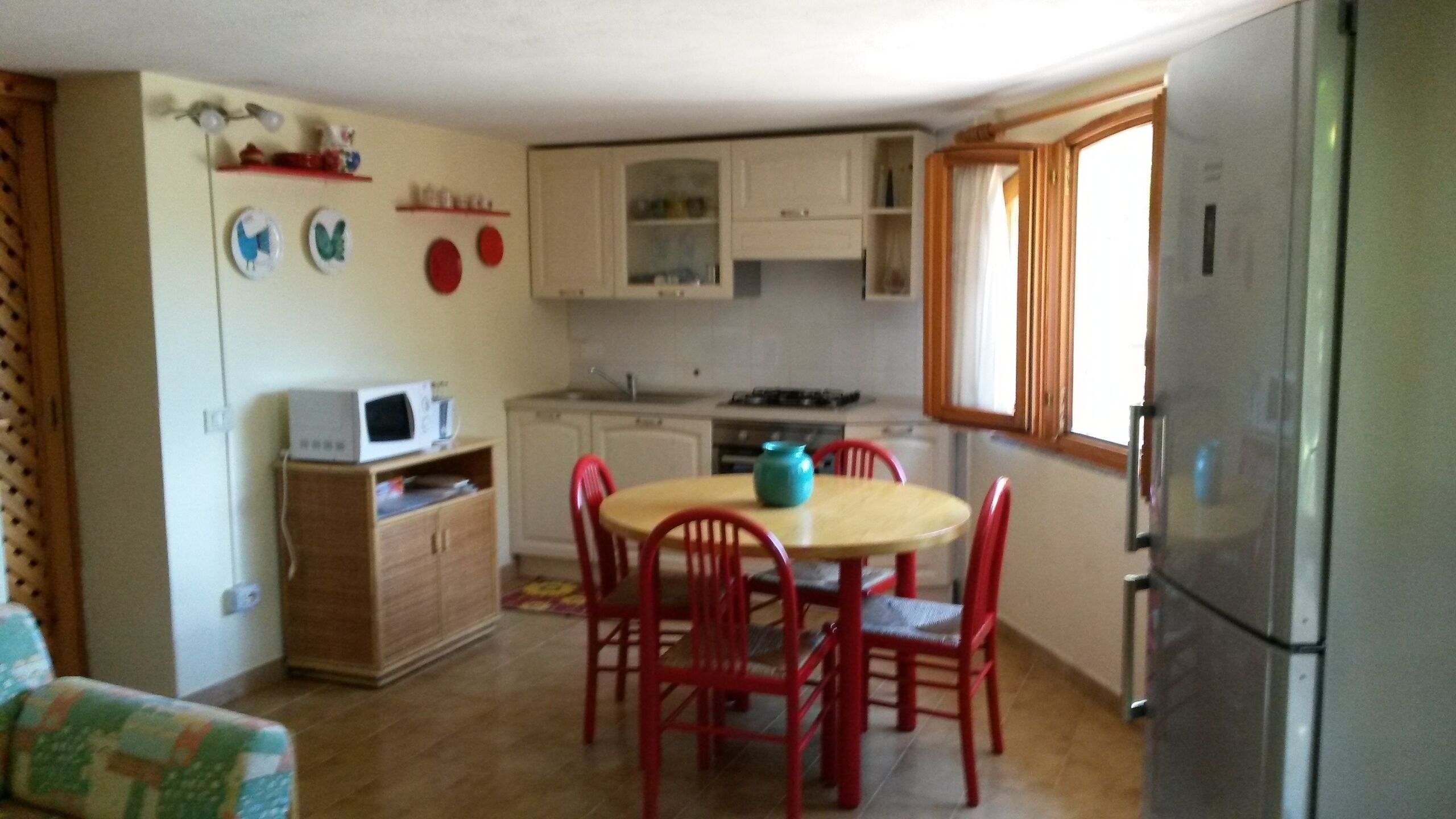 Een kleine keuken met een eettafel, stoelen, een magnetron, kastjes en een koelkast.