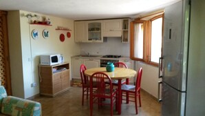 Een kleine keuken met een eettafel, stoelen, een magnetron, kastjes en een koelkast.