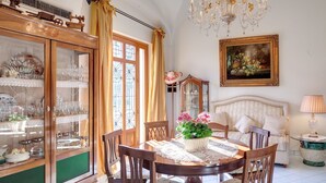 A dining room with a wooden cabinet, a chandelier, a painting, and a bed.