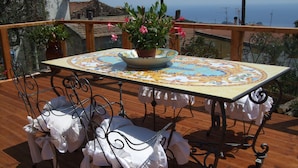 A wooden deck with a table and chairs, a potted plant, and a view of the sea.