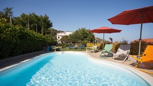 A swimming pool with clear water, surrounded by lounge chairs and umbrellas, and a building in the background.