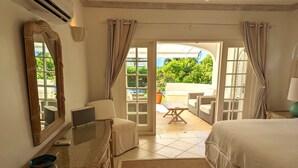 A bedroom with a bed, a dresser, a desk, and a chair. There is a window with curtains and a view of greenery outside. - A Luxurious Place To Chill Out In Barbados (Mount Standfast)