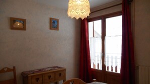 A bedroom with a wooden bed, a bedside table, and a window with red curtains.
