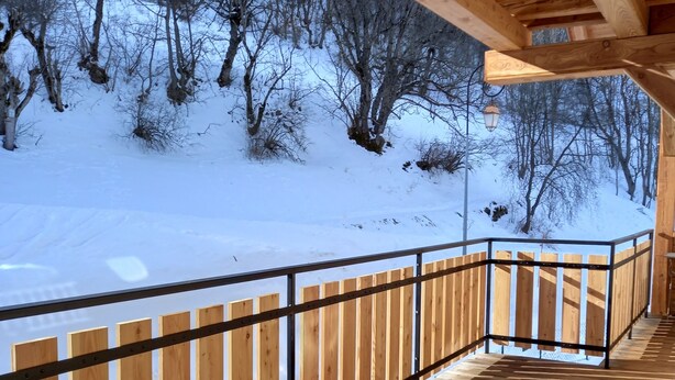 A wooden deck with a metal railing overlooking a snowy landscape.