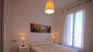 A bedroom with a bed, two bedside tables, a painting on the wall, and a window with curtains. - APARTMENT BARCELONA near BEACH (Barcelona)