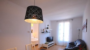 A modern living room with a dining table, a black sofa, a TV, and a large pendant light. - APARTMENT BARCELONA near BEACH (Barcelona)