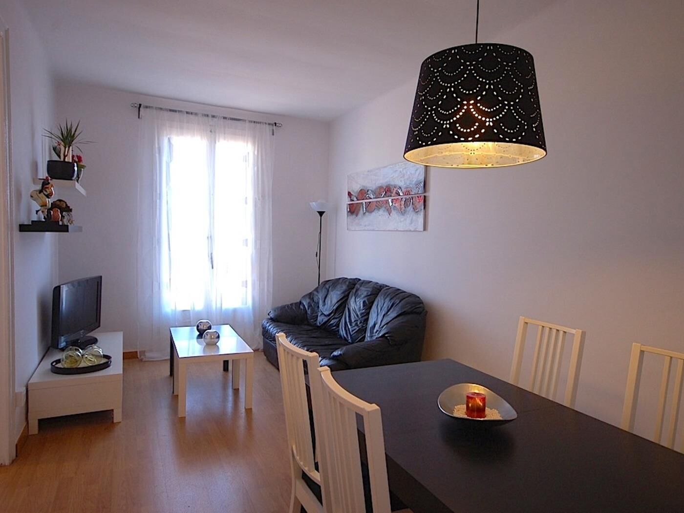A modern living room with a black leather sofa, a dining table with chairs, a TV on a stand, and a pendant light.
