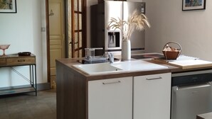 Eine Küche mit einer zentralen Kochinsel, Holzbalken an der Decke, einem Kühlschrank und einem Geschirrspüler.